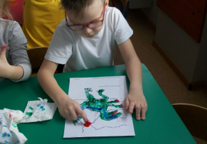 Julek maluje farbami dinozaura.