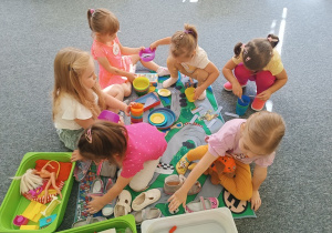 Dziewczynki urządzają piknik na dywanie.