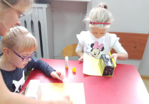 Gabrysia i Olga przyklejają kolorowy papier do pudełek.