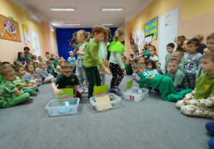 Dzieci segregują śmieci do odpowiednich pojemników.