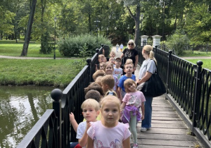 Przedszkolaki przechodzą przez mostek w parku.