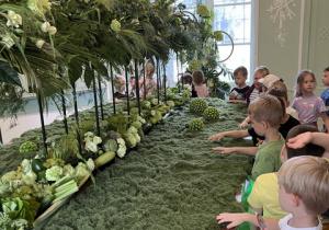 Przedszkolaki przyglądają się pięknej wystawie roślin, owoców i warzyw.