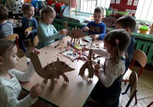 Dzieci przy stoliku ozdabiają sylwety dinozaury.