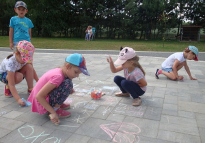 Dziewczynki rysują kredą na chodniku.