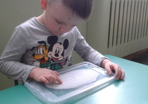Chłopiec rysuje palcem w soli.