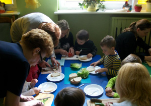 Rodzice i dzieci z dużym zaangażowaniem przygotowują kanapki.