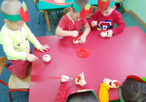Pawełek, Igor i Kuba malują swoje jabłuszko czerwona farbą.