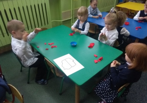 Dzieci kręcą kuleczki z czerwonej bibuły.