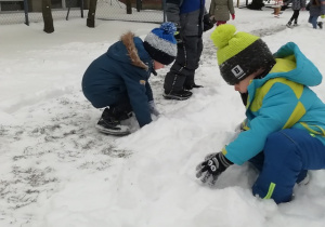 Chłopcy toczą kule śniegowe.