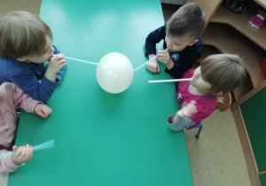 Dzieci dmuchają na balon przez słomkę - trąbę słonia.
