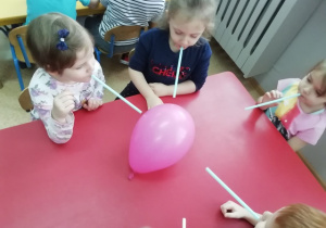 Dziewczynki starają się przesunąć balon dmuchając przez słomkę - trąbą słonia.