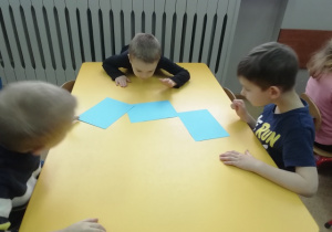 Dzieci wprawiają w ruch kartki na stoliku żółtym - ćwiczenia oddechowe.