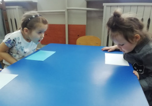 Dzieci wprawiają w ruch kartki na stoliku niebieskim - ćwiczenia oddechowe.