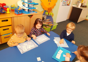Dzieci przy stoliku niebieskim układają elementy pogody.