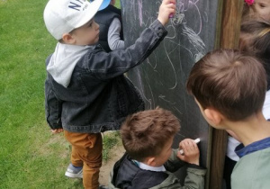 Chłopcy rysują kolorową kredą po tablicy.