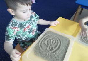 Fabian prezentuje swój rysunek na piasku.