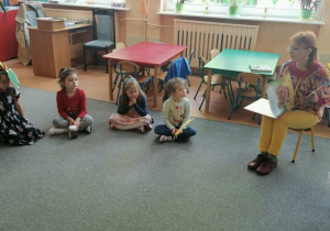 Dzieci uważnie słuchają książki czytanej przez p. Katarzynę z biblioteki.