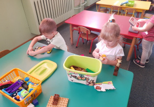 Hania i Gabryś bawią się przy stoliku zabawkami.