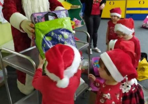 Mikołaj obdarowuje dzieci prezentami.