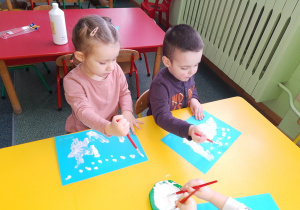 Laura i Miłosz malują krajobraz zimowy białą farbą.