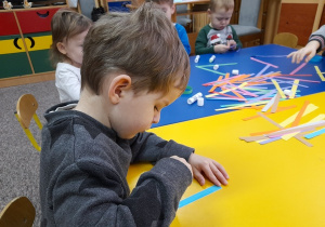 Dzieci sklejają paski papieru kolorowego.