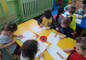 Dzieci siedzący przy stoliku żółtym malują trawę.