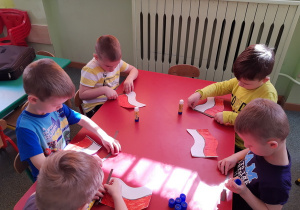 Dzieci przy stoliku czerwonym wykonują swoje flagi.