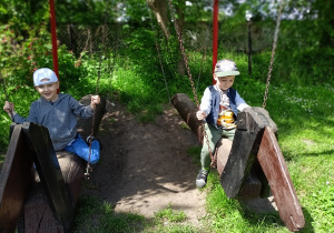 Hubert i Olek ćwiczą jazdę na koniach drewnianych.