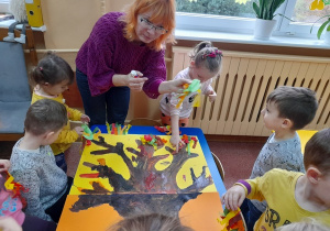 Dzieci przyklejają listki do pomalowanego drzewa