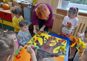 Dzieci przyklejają listki do pomalowanego drzewa