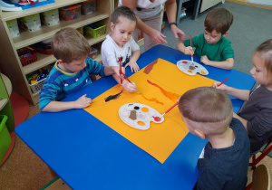 Dzieci malują pień drzewa.