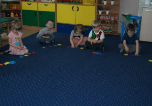 Dzieci siedzą na dywanie i nazywają figury,