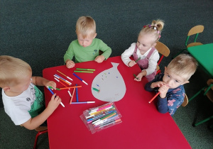 Dzieci przy czerwonym stoliku wspólnie ozdabiają kartkę w kształcie balonu.