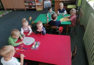 Dzieci z zielonego stolika z uśmiechami na buzi obmyślają jak ozdobić balonik z kartki