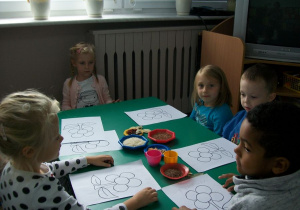 Dzieci przy stoliku zielonym zainteresowaniem oglądają różne przyprawy.