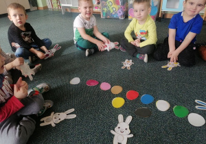 Dzieci siedzą na dywanie i nazywają kolory.