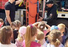 Strażacy tłumaczą dzieciom do czego służą nosze będące na wyposażeniu w wozie strażackim.