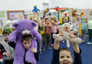 Dzieci trzymają misie nad głowami.